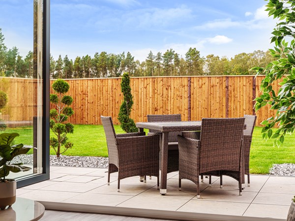A photograph of a brown patio table and chairs in the garden of a home.